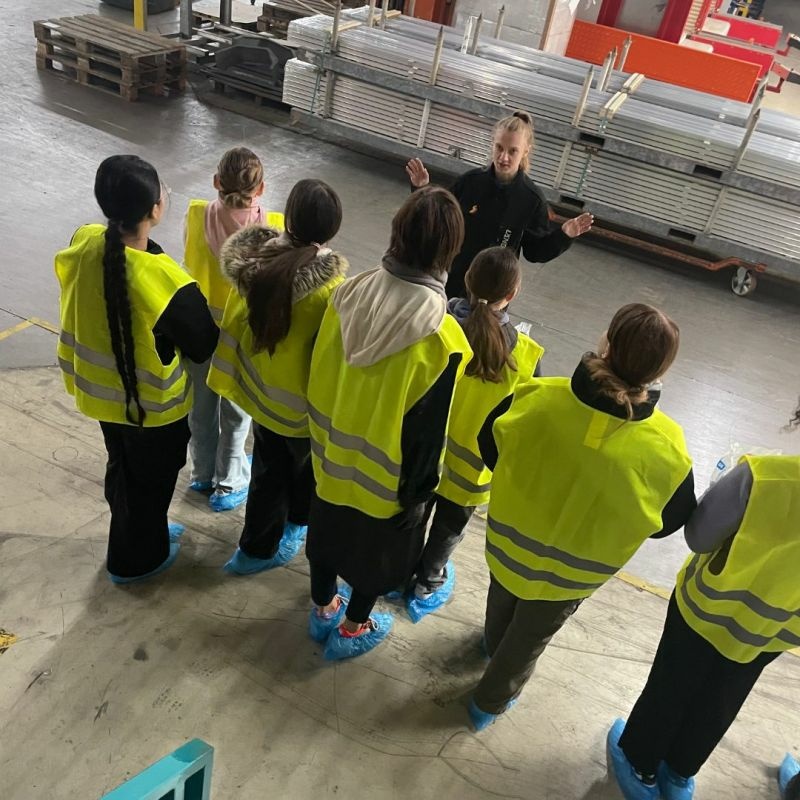 Eine Gruppe junger Besucherinnen in Warnwesten und Überschuhen bekommt eine Führung durch die Produktionshalle von Längle Oberflächen.