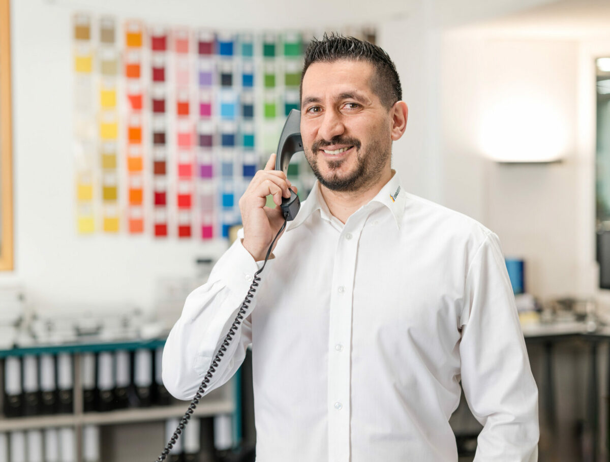 Mitarbeiter im Kundenservice hat Kontakt mit Kunden im Büro mit Farbmustern im Hintergrund.