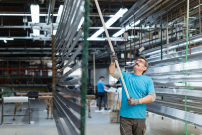 Mitarbeiter überprüft die gleichmäßige Aufhängung von Aluminiumprofilen vor der Pulverbeschichtung.