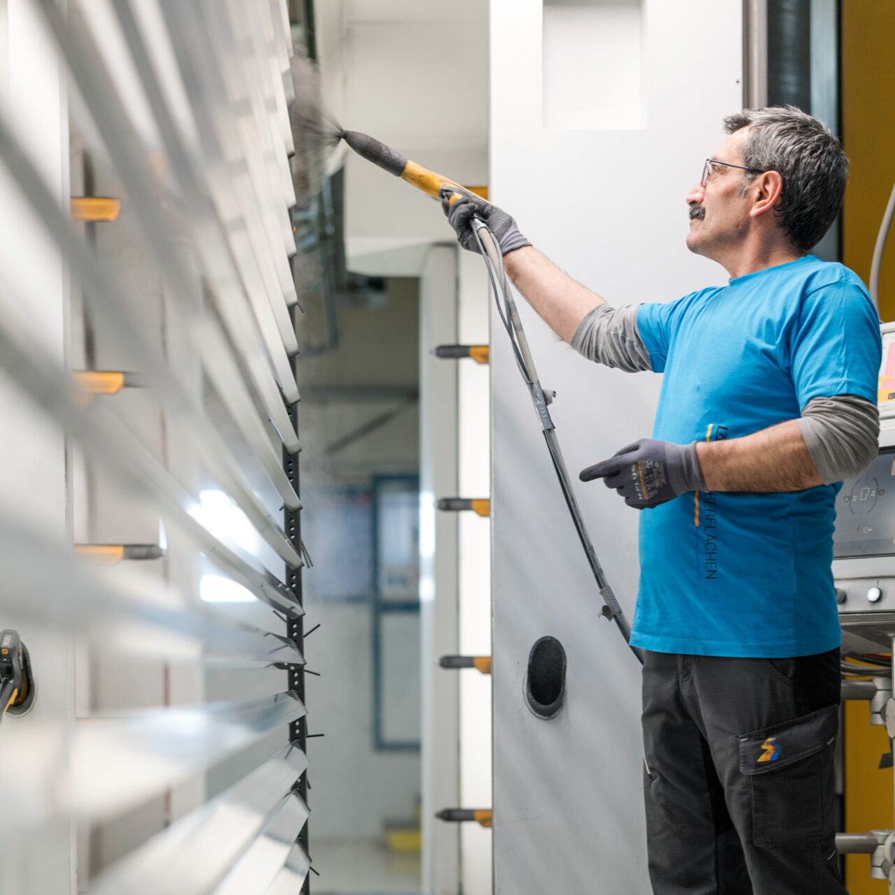 Facharbeiter trägt Pulverbeschichtung auf Aluminiumlamellen auf.