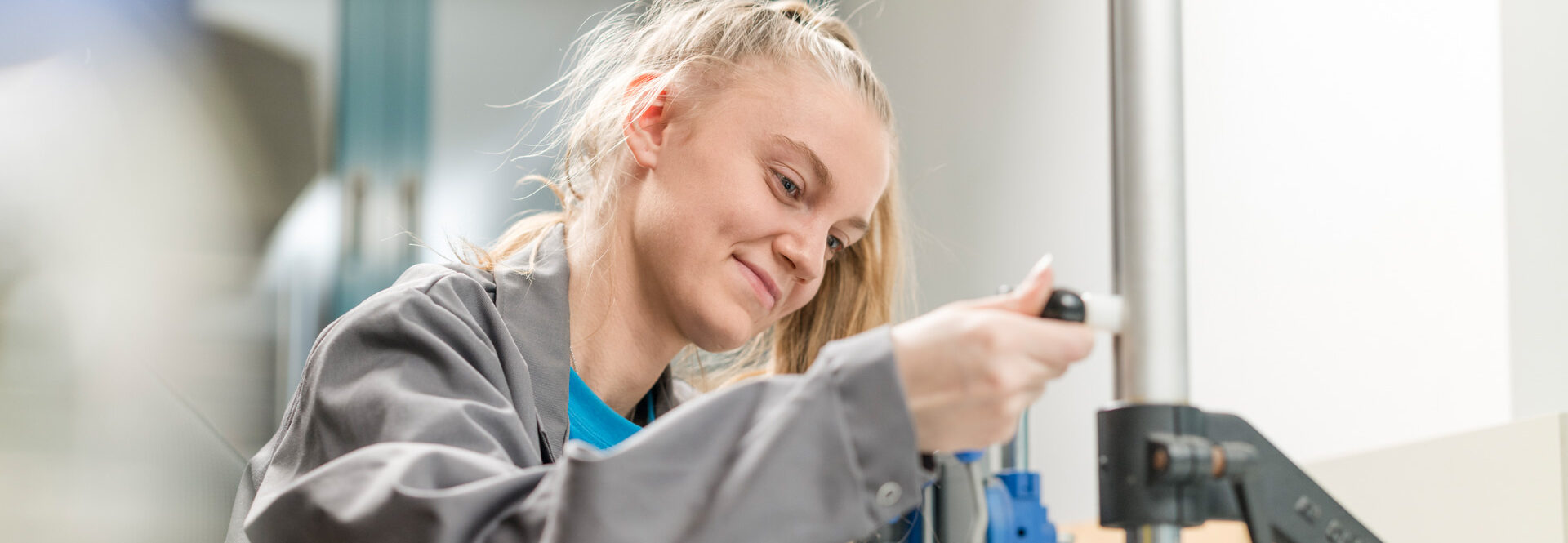 Eine junge Frau in grauer Arbeitskleidung führt eine Qualitätsprüfung an einer beschichteten Oberfläche durch.