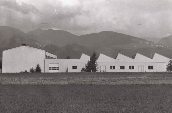 Ehemaliges Produktionsgebäude von Längle Oberflächen mit markanter Dachstruktur, umgeben von Landschaft und Bergen.