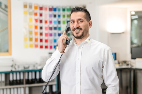 Mitarbeiter im Kundenservice hat Kontakt mit Kunden im Büro mit Farbmustern im Hintergrund.