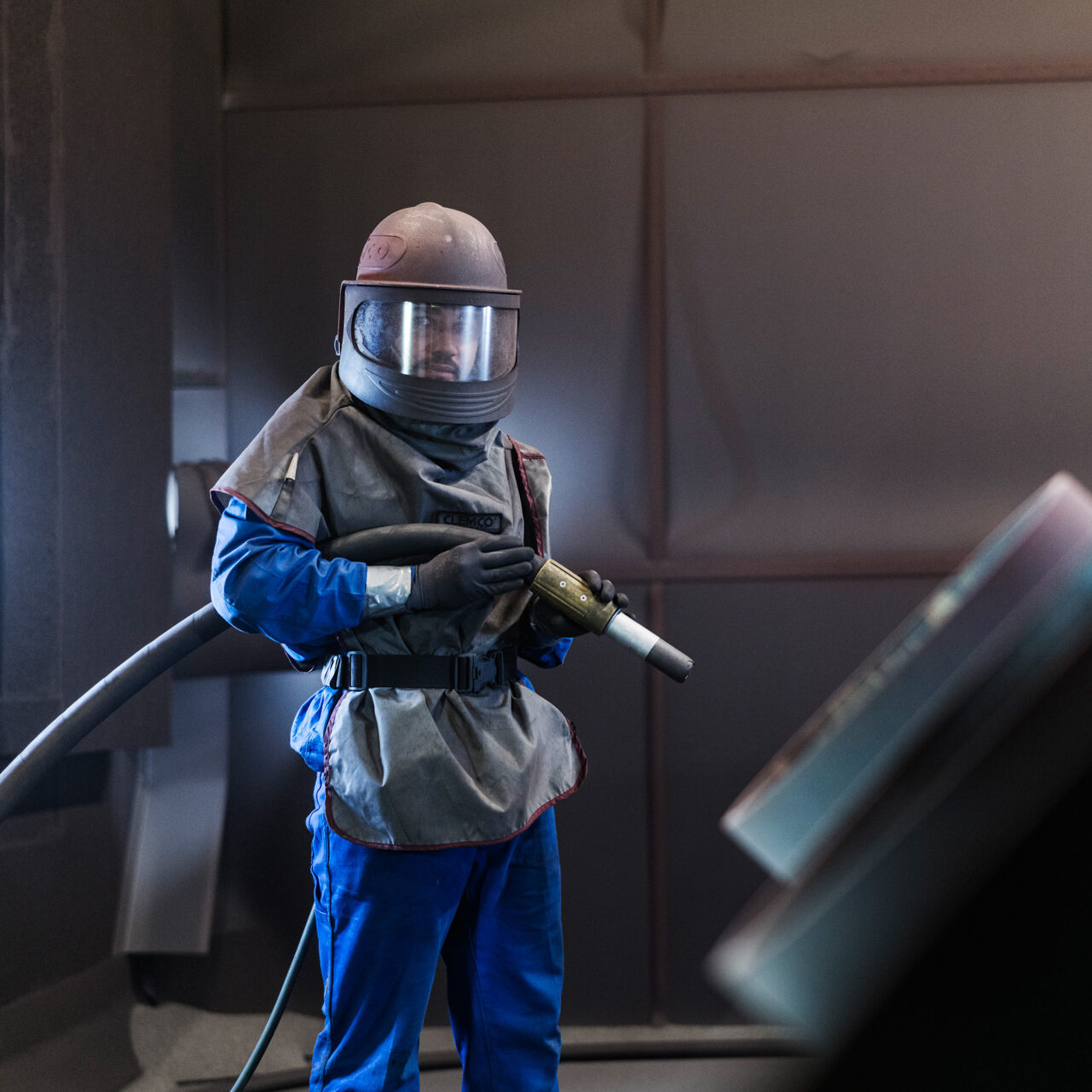 Fachkraft beim Sandstrahlen mit Schutzanzug und Strahlpistole.