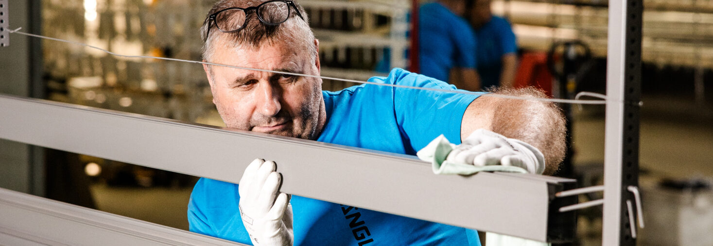 Mitarbeiter von Längle Oberflächen prüft und reinigt ein pulverbeschichtetes Aluminiumprofil für höchste Qualitätsstandards.
