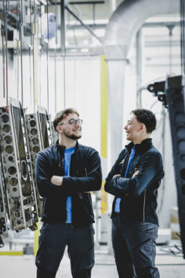 Zwei Jungs in der Produktionshalle von Längle Oberflächen absolvieren die Lehre und stehen vor Metallbauteilen