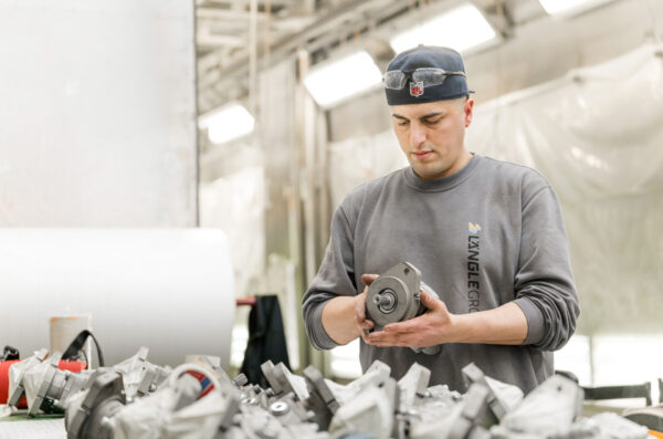 Mitarbeiter prüft ein metallisches Bauteil in einer Produktionshalle.
